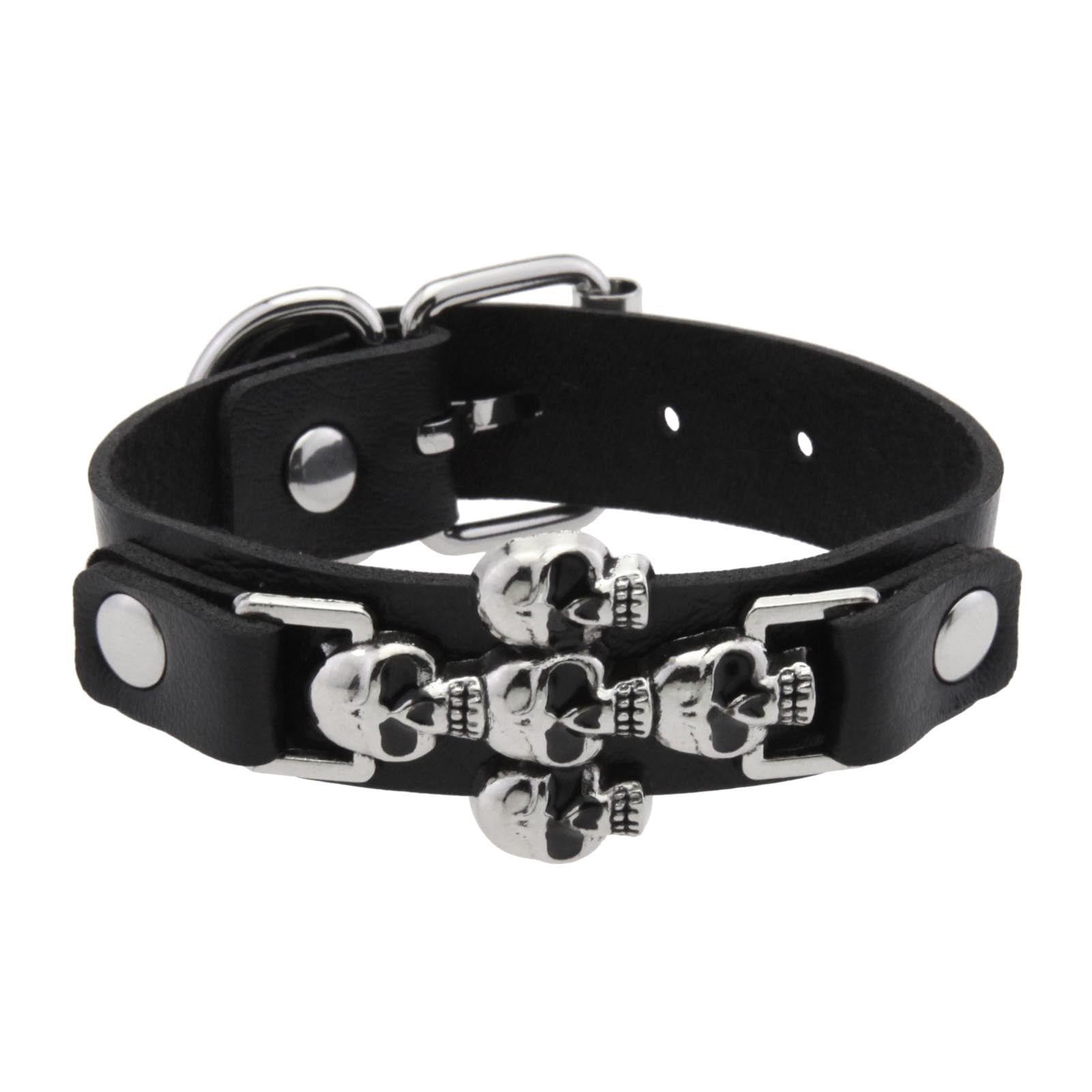 Brazalete de piel sintética negra con adorno central de múltiples calaveras plateadas.
