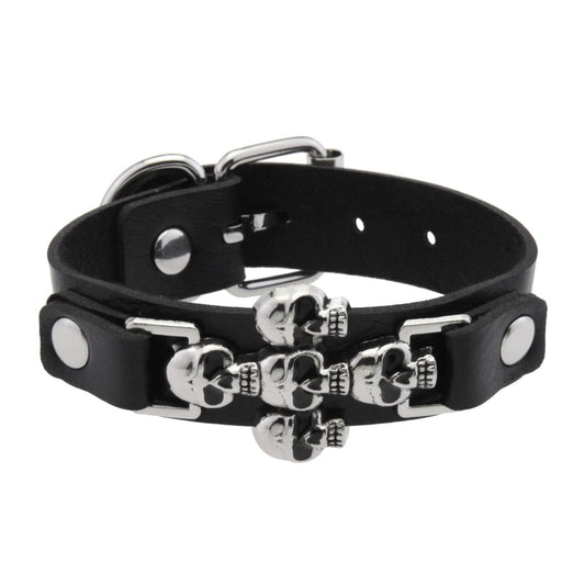 Brazalete de piel sintética negra con adorno central de múltiples calaveras plateadas.