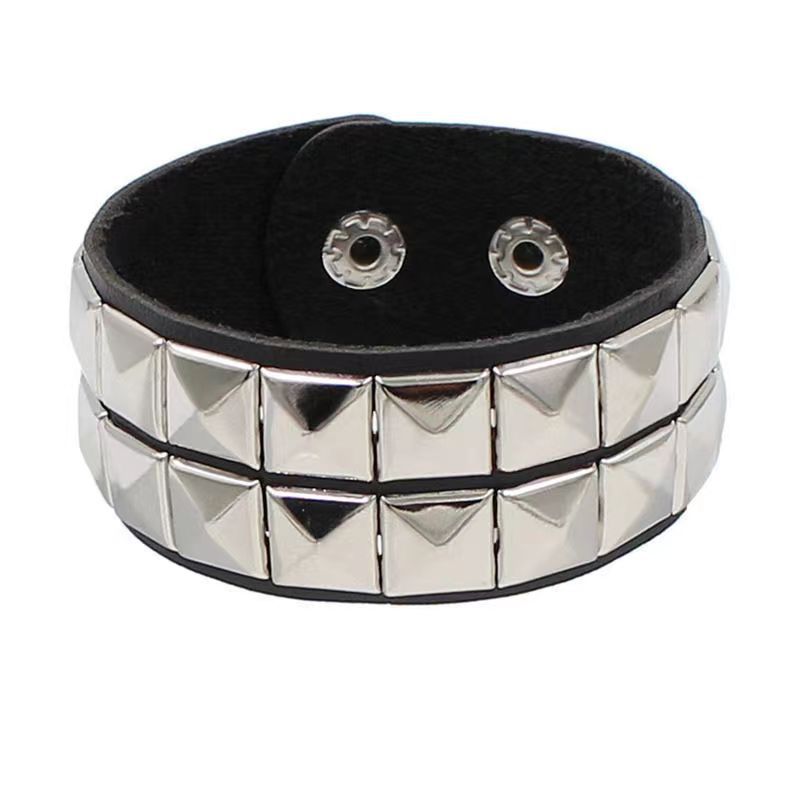 Vista frontal de brazalete de piel sintética negra con doble fila de tachuelas cuadradas plateadas.