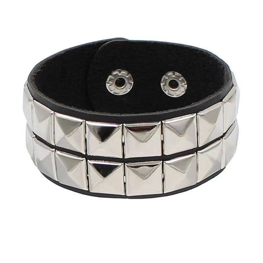 Vista frontal de brazalete de piel sintética negra con doble fila de tachuelas cuadradas plateadas.